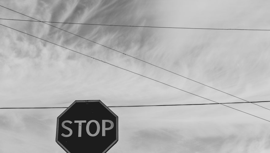 greyscale image of a stop sign with the sky and phone lines in the background.